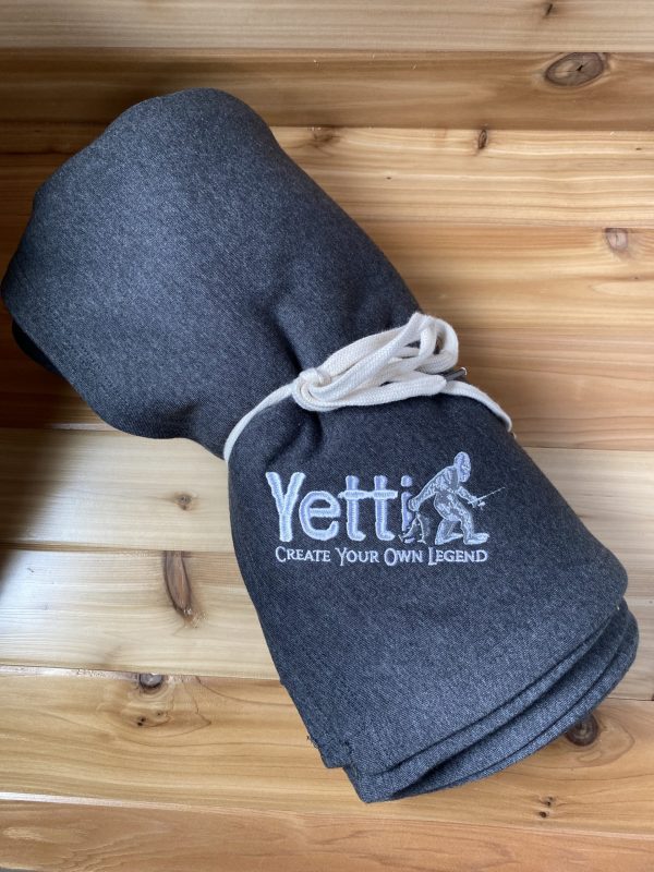 Gray rolled up blanket tied with a white bow with a white Yetti Fish House logo on the blanket